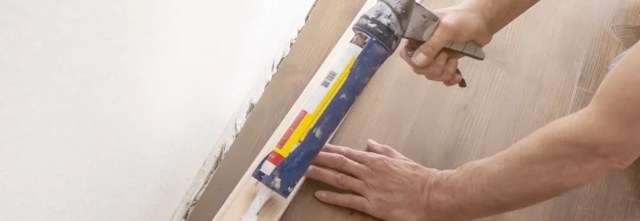 Person trägt Dichtmittel auf Sockelleiste auf